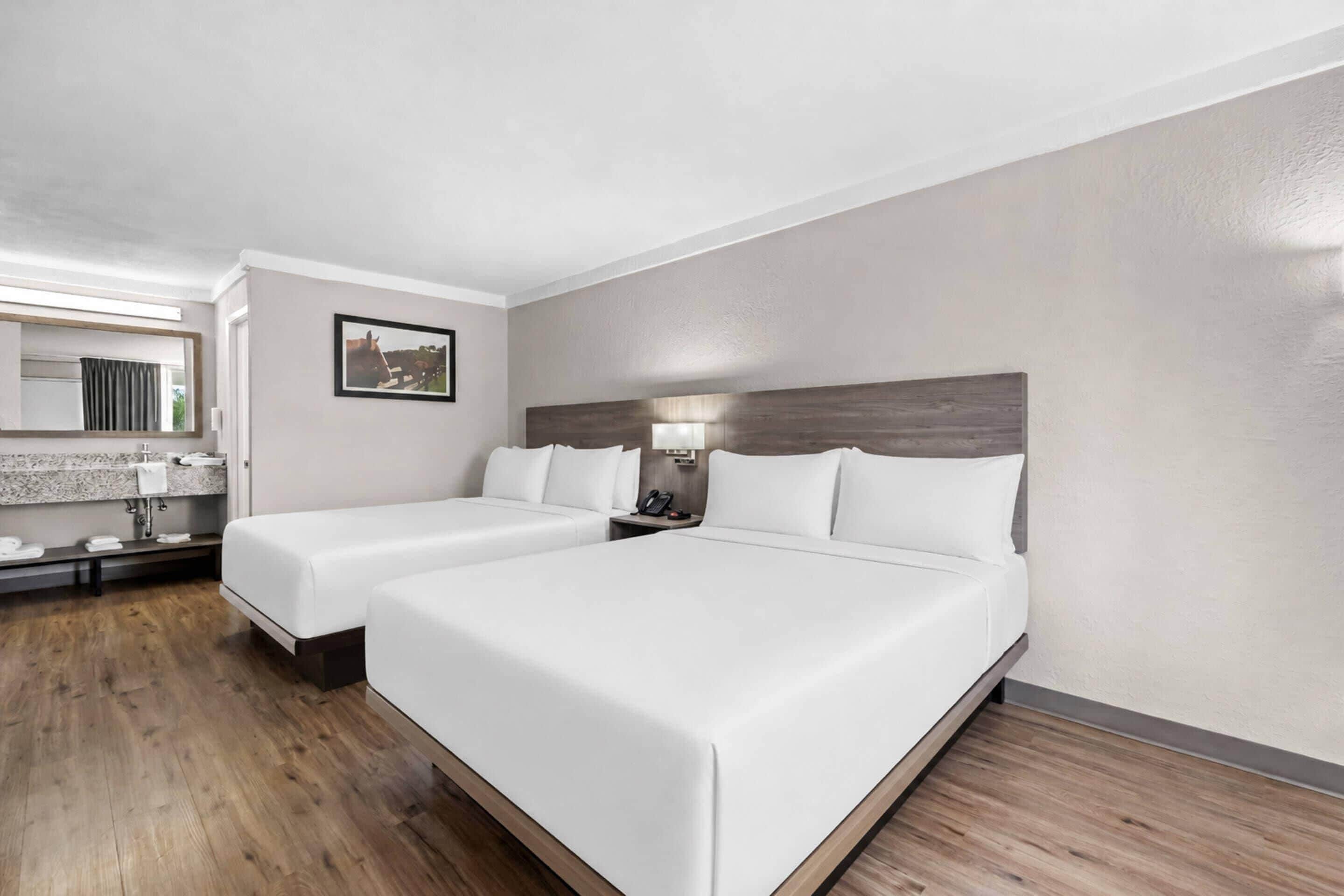 A hotel room with two beds, a bathroom with a mirror, and a picture on the wall.