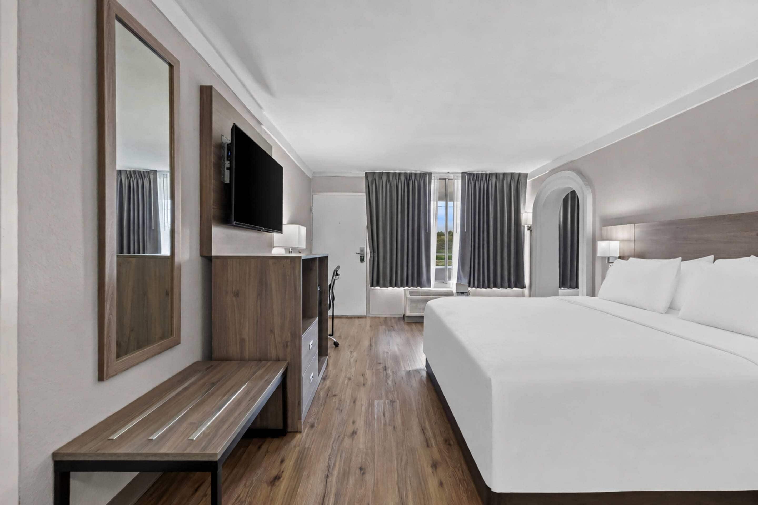A hotel room with a large bed, a desk with a chair, a television, and a window with curtains.