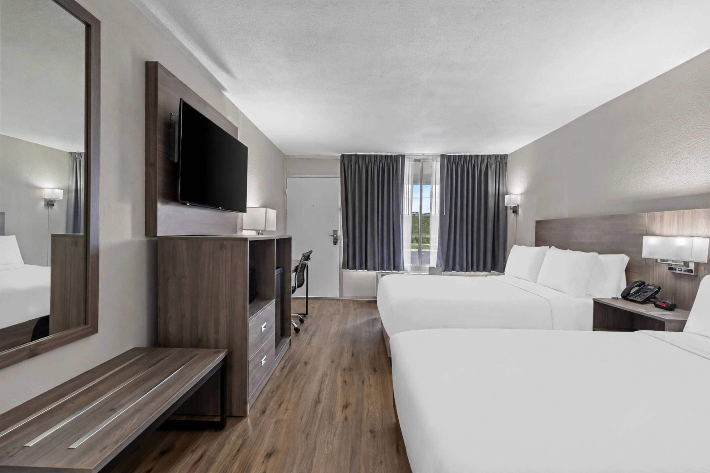A hotel room with a large bed, a smaller bed, a desk, a TV, and a window with curtains.