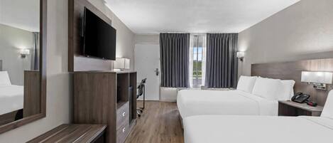 A hotel room with a large bed, a smaller bed, a desk, a TV, and a window with curtains.