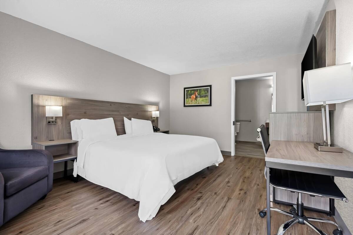 A hotel room with a large bed, a desk with a chair, a sofa, and a wooden headboard.