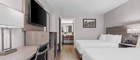A hotel room with a bed, a desk, a TV, a mirror, and a bathroom visible through an open door.