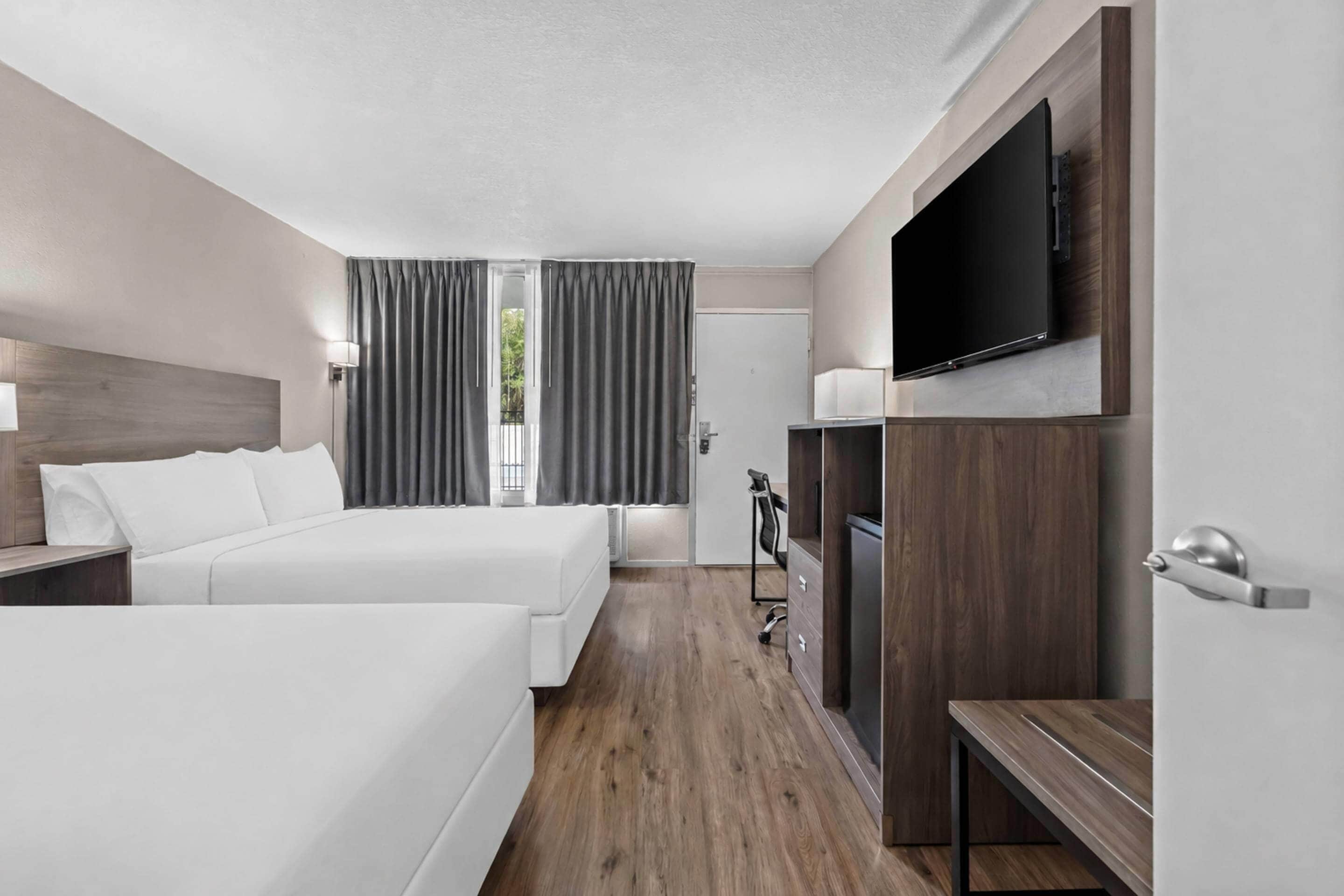 Habitación de hotel con dos camas, televisión, escritorio y ventana con cortinas.