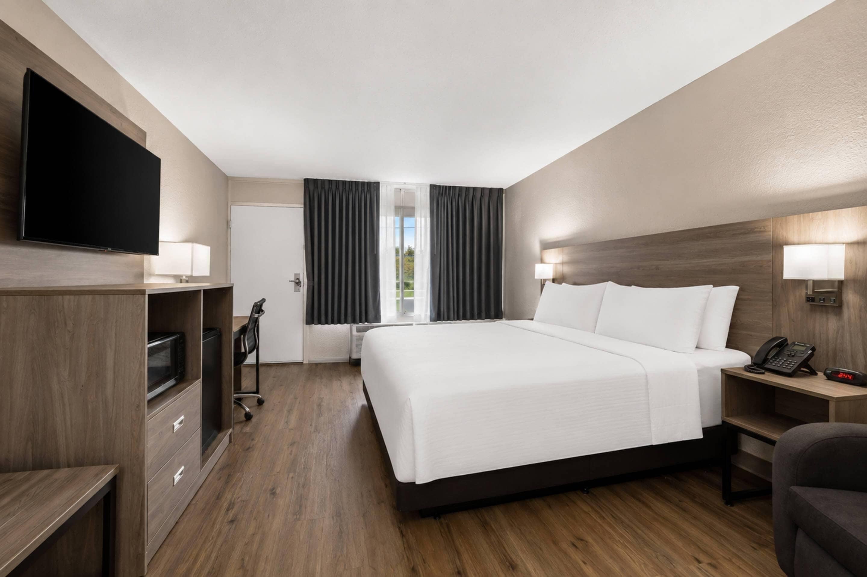 A hotel room with a bed, a desk, a chair, a TV, and a window with curtains.