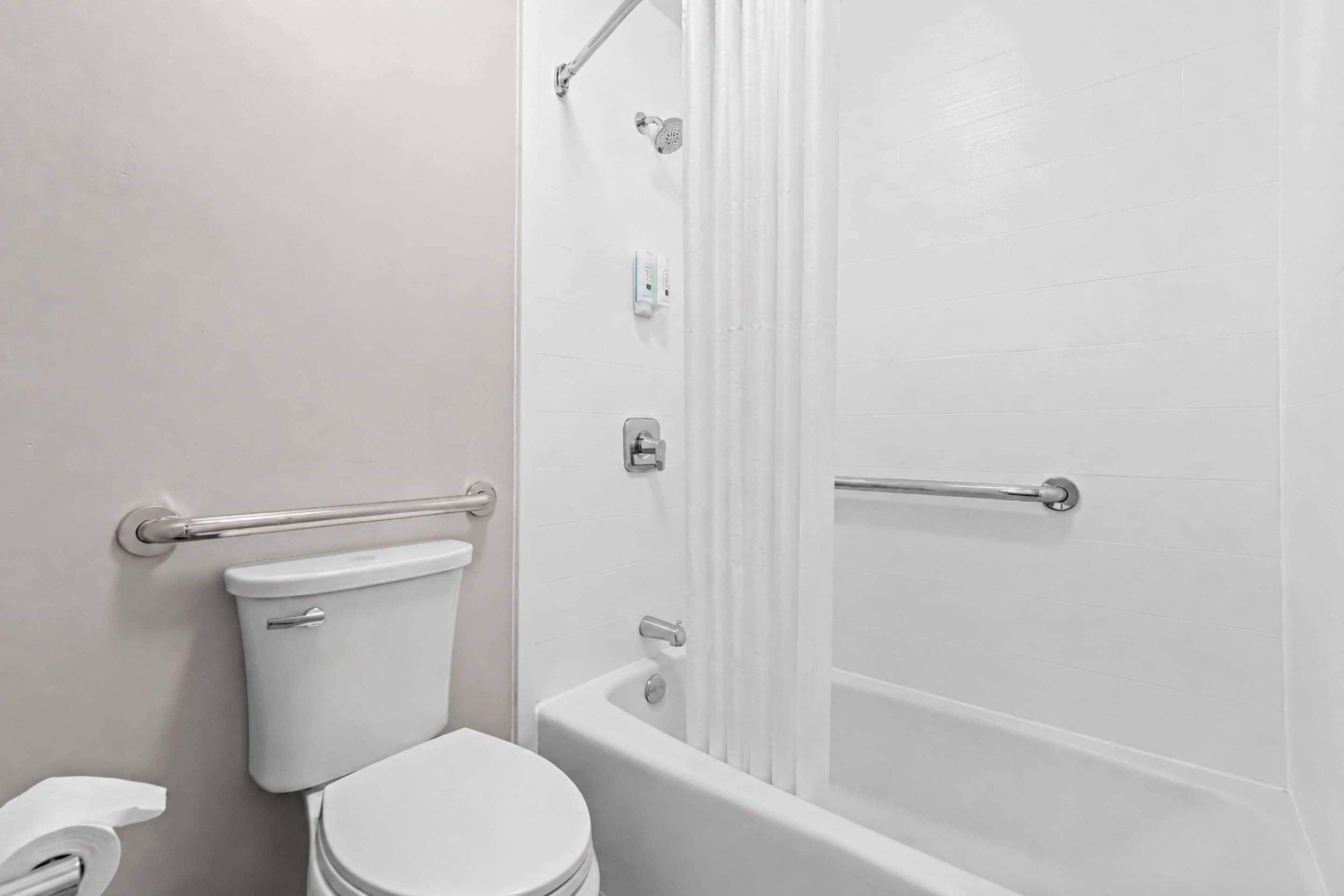 A bathroom with a toilet, a handrail, a shower curtain, and a bathtub.