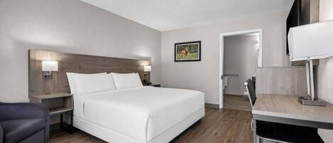 A hotel room with a bed, bedside tables, a desk, a chair, and a television.