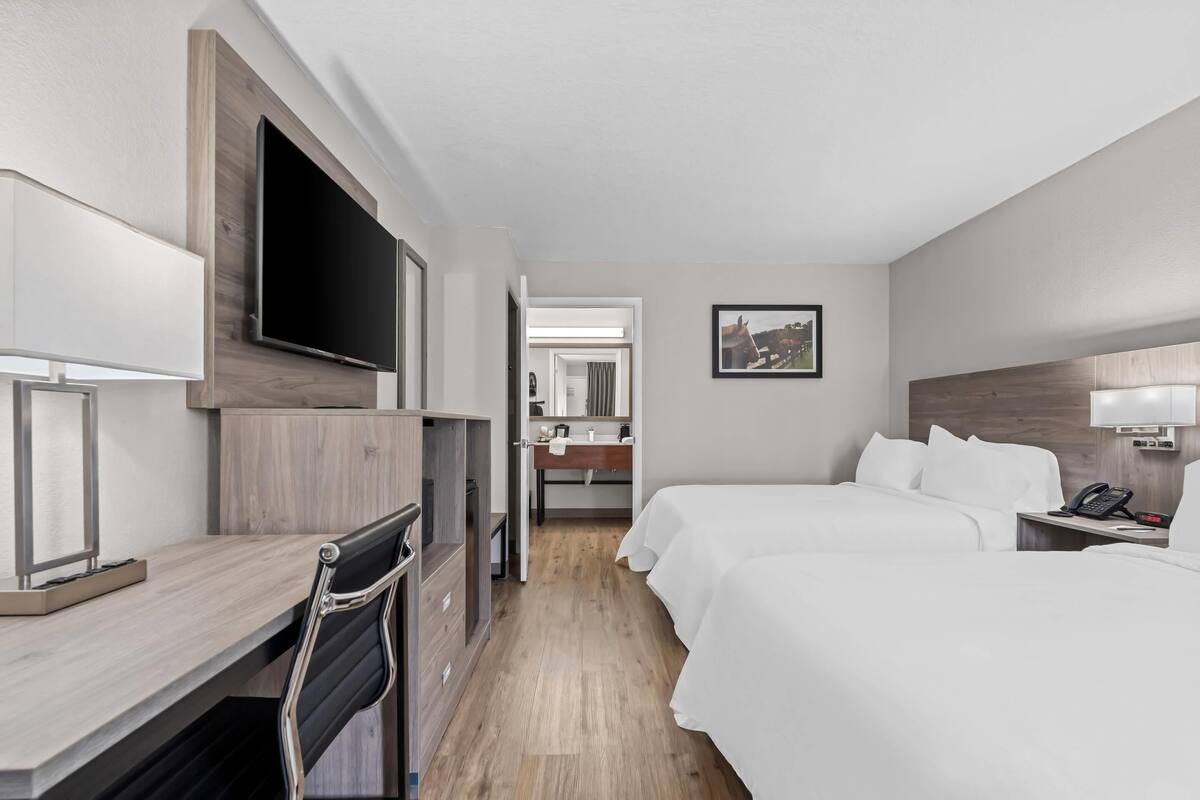 A hotel room with a desk, two beds, a TV, a mirror, and a phone.