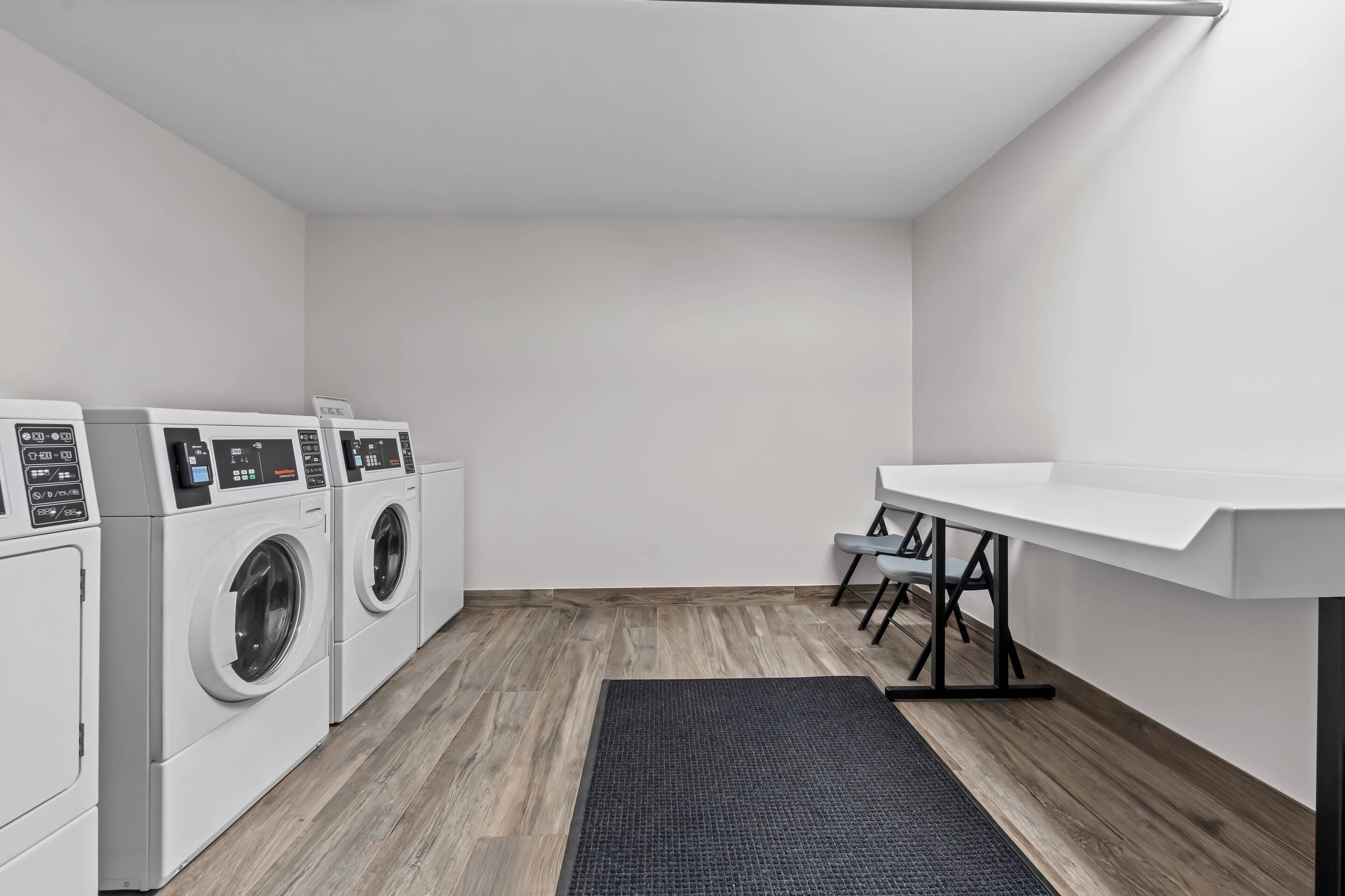 Een wasserette met een wasmachine, droger en een tafel met stoelen.