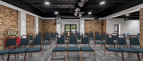 A conference room with rows of chairs, a brick wall, and a large window.