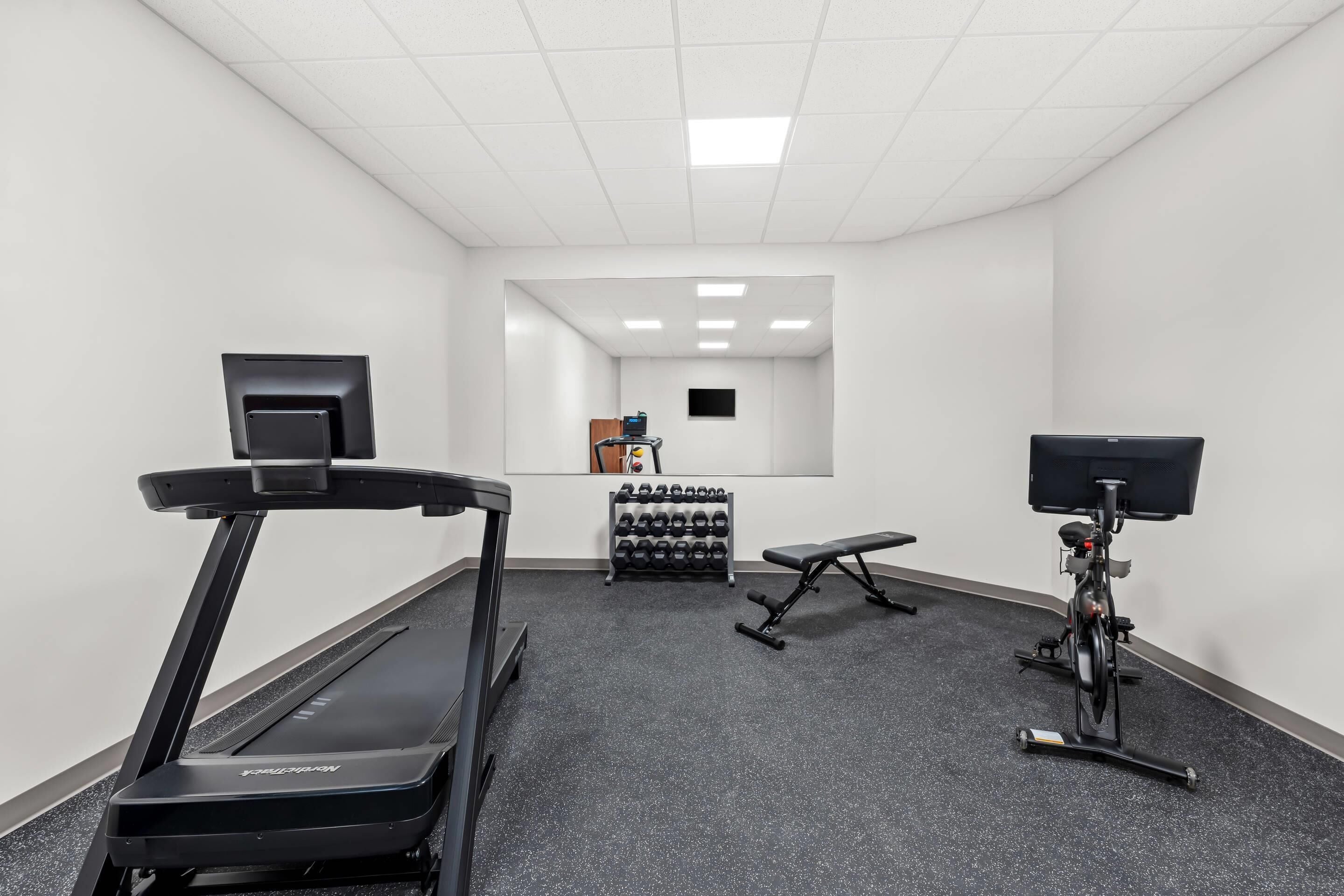 Un gimnasio con cintas de correr, una bicicleta estática y un banco.