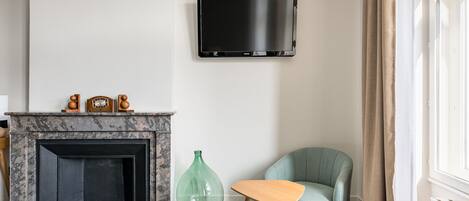 Un salon avec une cheminée, un téléviseur fixé au mur, un vase vert et un fauteuil turquoise.