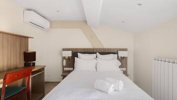 Quarto de hotel com cama, escrivaninha, cadeira, luminária e ar condicionado.