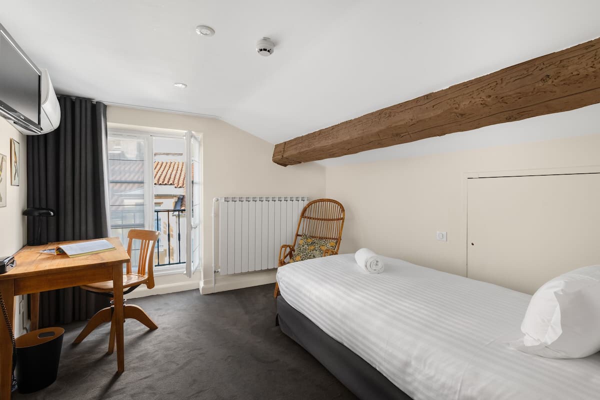 A bedroom with a bed, a wooden desk, a chair, a radiator, and a window with curtains.