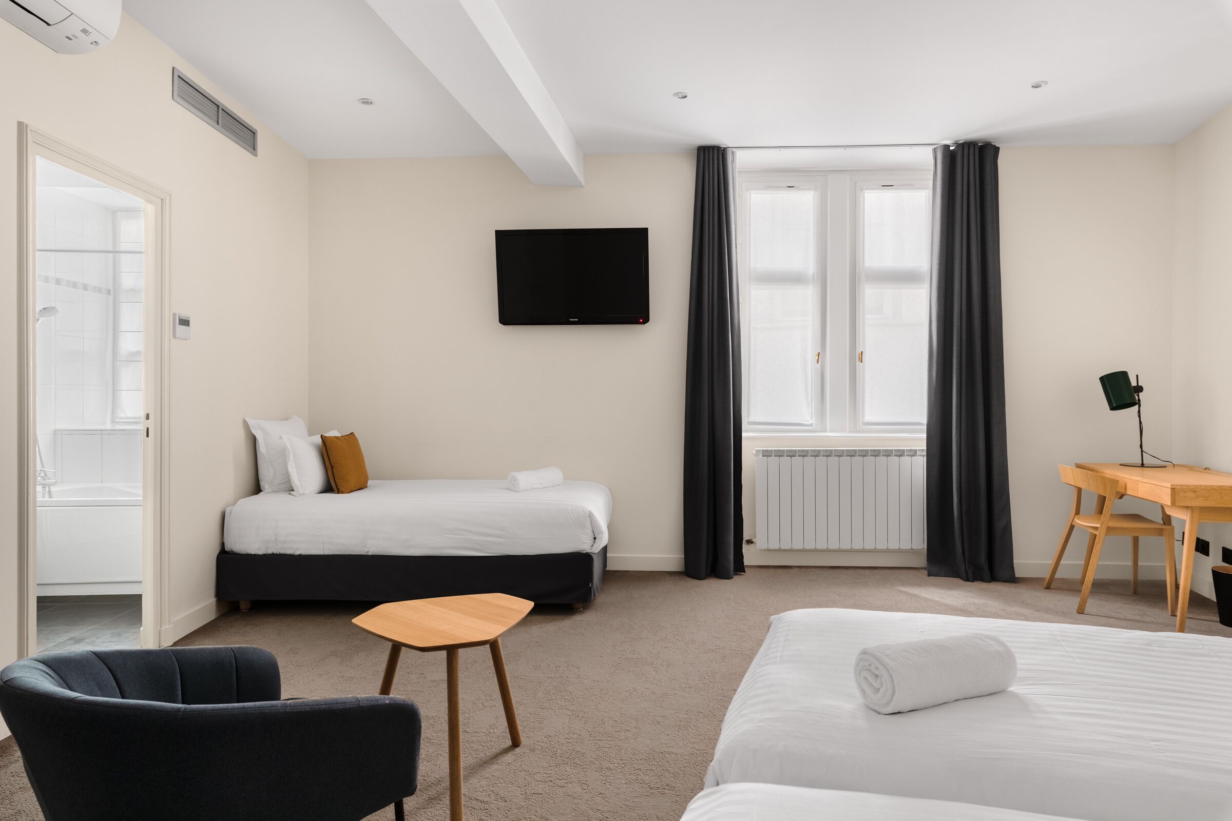 Une chambre d’hôtel avec deux lits, un bureau, une chaise, une télévision et une fenêtre avec des rideaux.