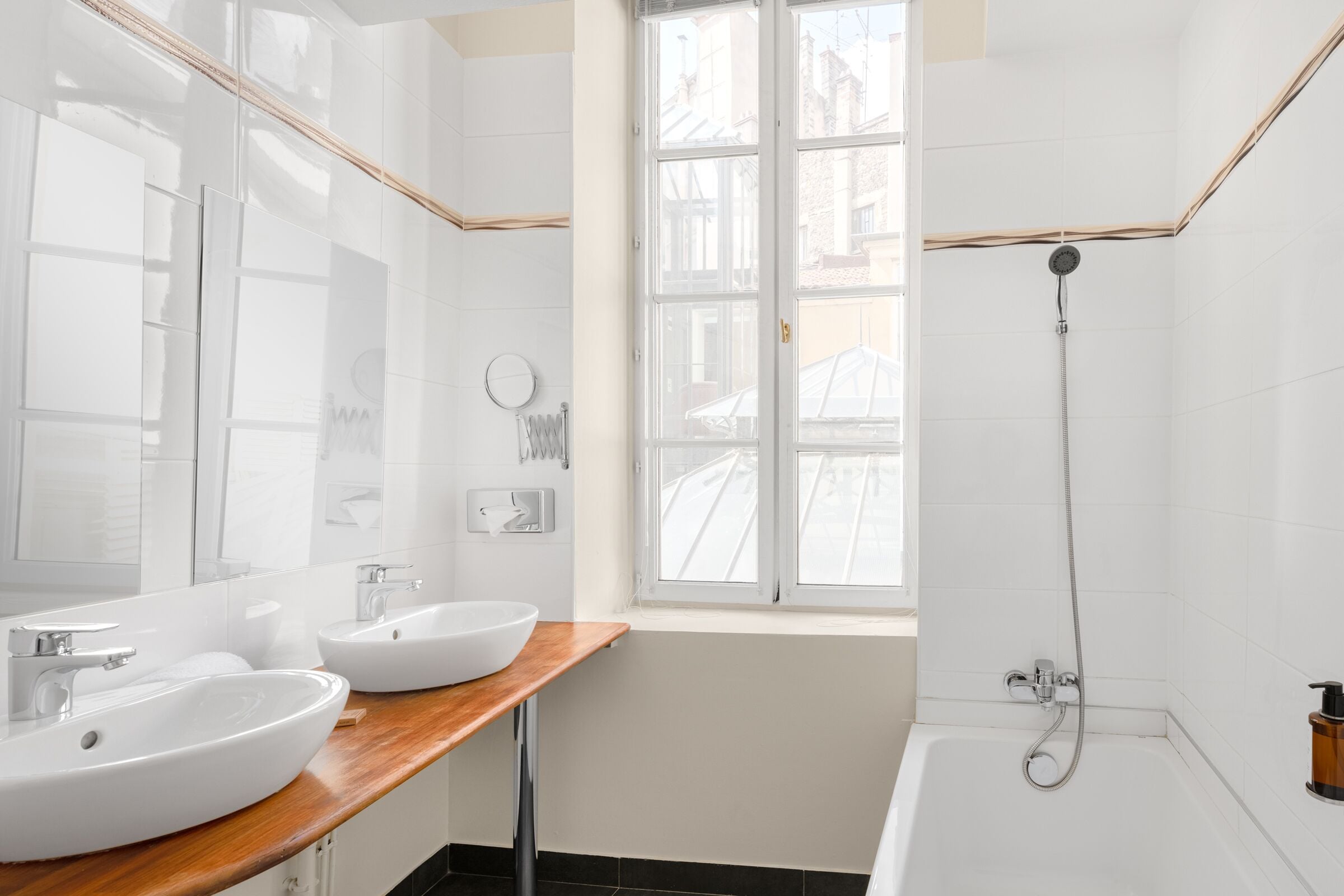 A modern bathroom with two sinks, a bathtub, and a window.