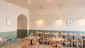 A dining area with multiple tables and chairs, framed artwork on the walls, and pendant lighting.