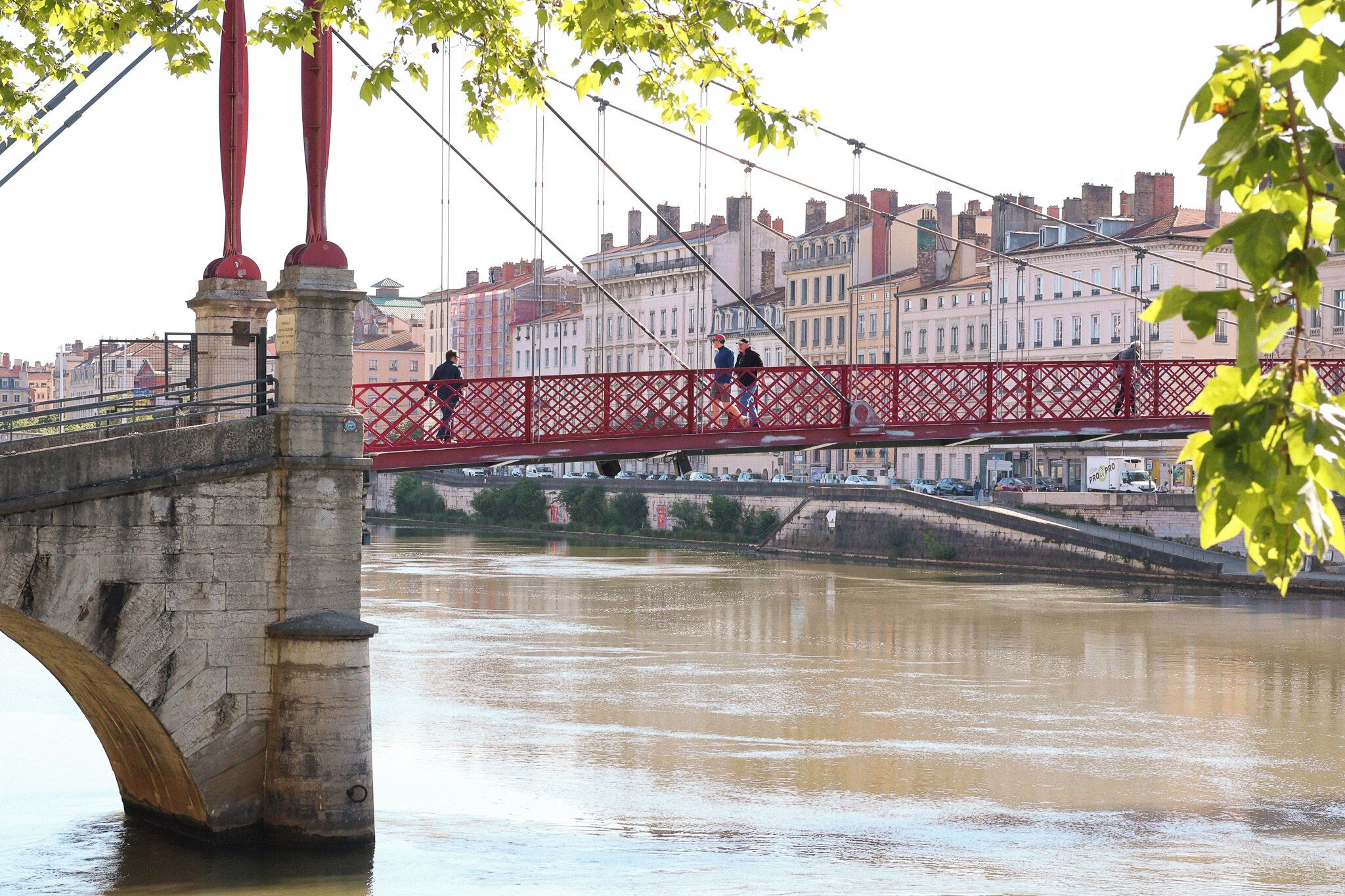 Un puente de piedra con barandilla roja sobre un río, con edificios al fondo.