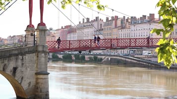 A stone bridge with a red railing over a river, with buildings in the background.