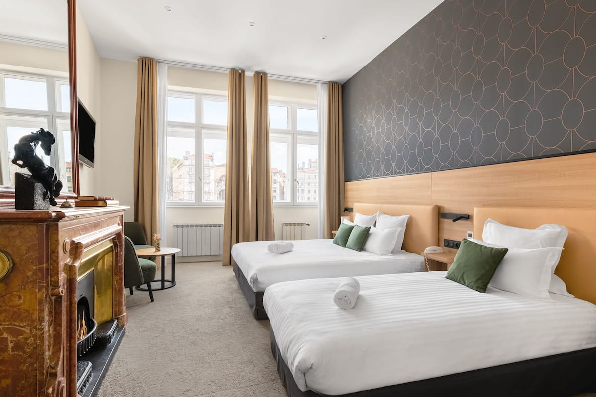 A hotel room with two beds, a fireplace, a television, and large windows with curtains.