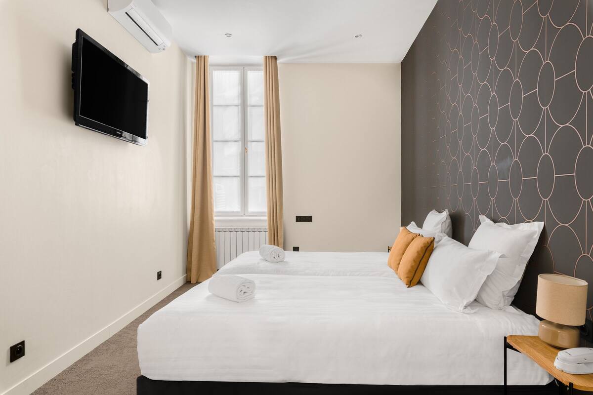 A hotel room with a large bed, a flat-screen TV mounted on the wall, a window with curtains, and a patterned wall.