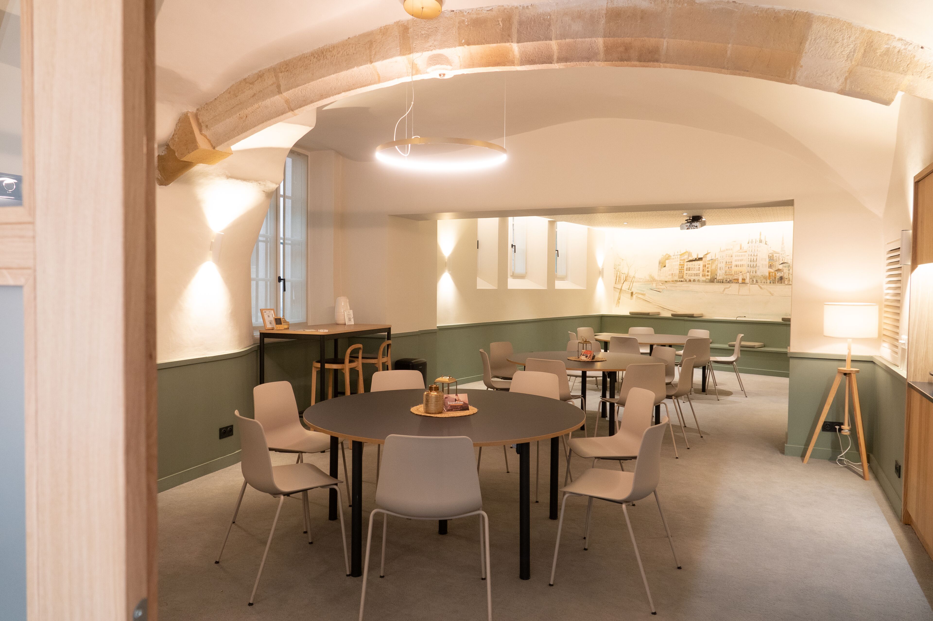 Une salle de conférence dotée de tables et de chaises rondes, d’un plafond en forme d’arc en pierre et offrant une vue sur le paysage urbain à travers les fenêtres.