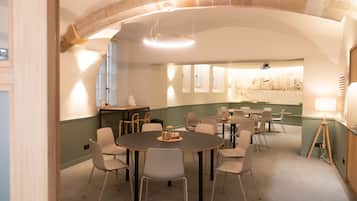 Une salle de conférence dotée de tables et de chaises rondes, d’un plafond en forme d’arc en pierre et offrant une vue sur le paysage urbain à travers les fenêtres.