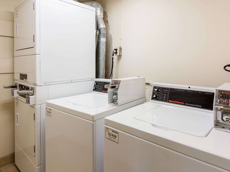 A laundry area with two white washing machines and a dryer, a vent pipe, and a control panel.