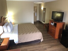 Una habitación de hotel con una cama, televisor, cómoda y espejo.