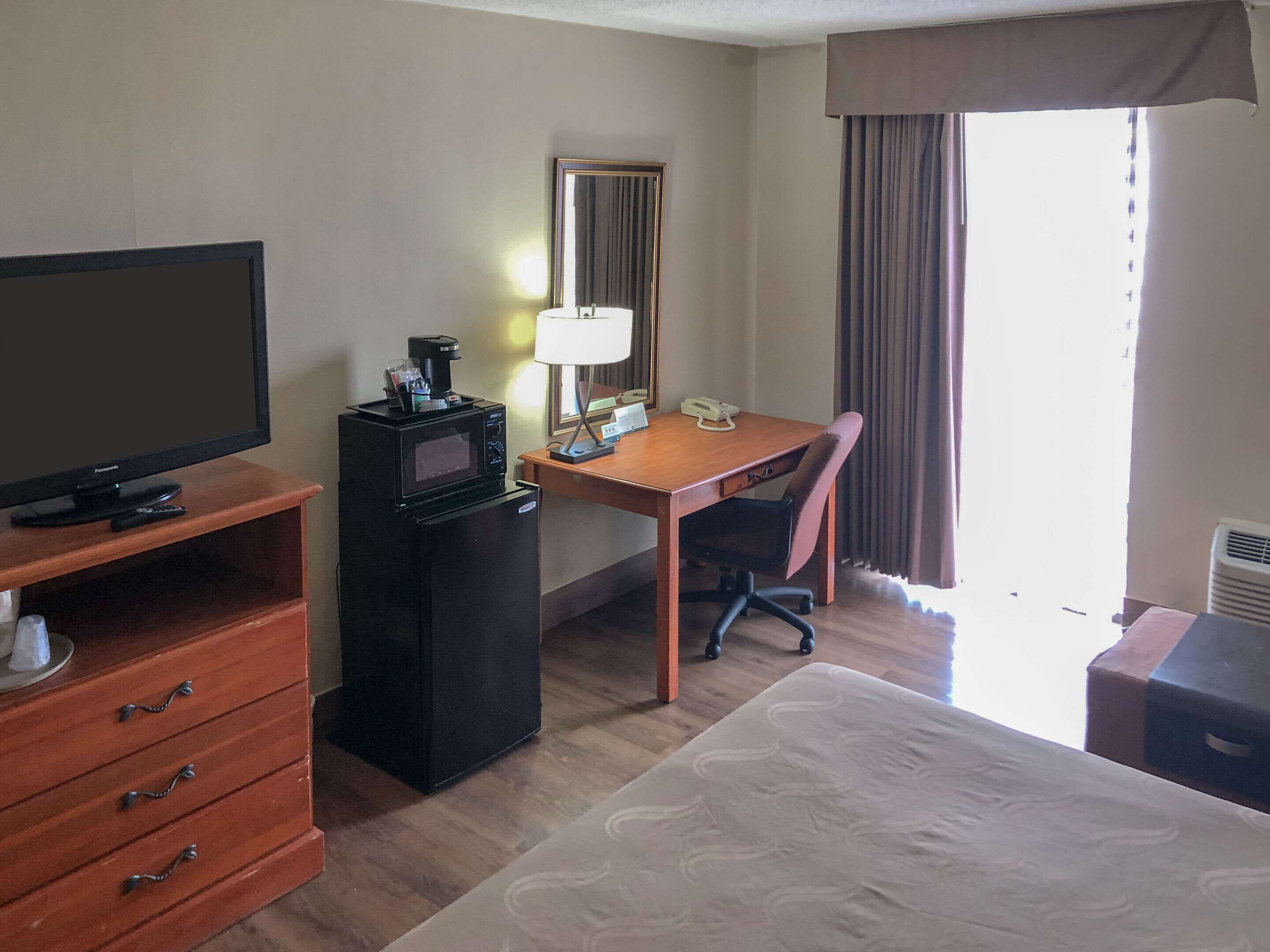 A hotel room with a bed, a desk with a chair, a television, a microwave, a telephone, and a dresser.