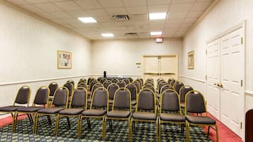 Un salón de conferencias con filas de sillas, piso alfombrado y una puerta a la derecha.