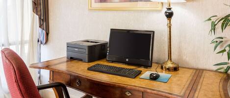 Un escritorio de hotel con una computadora de escritorio, una impresora, una lámpara y una silla roja.