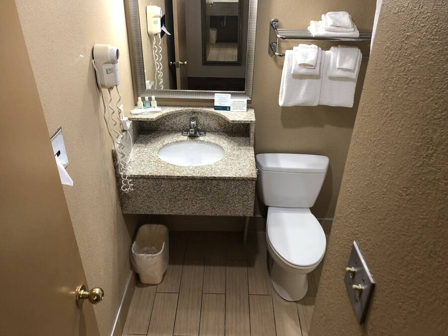 Baño de hotel pequeño con lavamanos de granito, inodoro y un perchero para toallas.