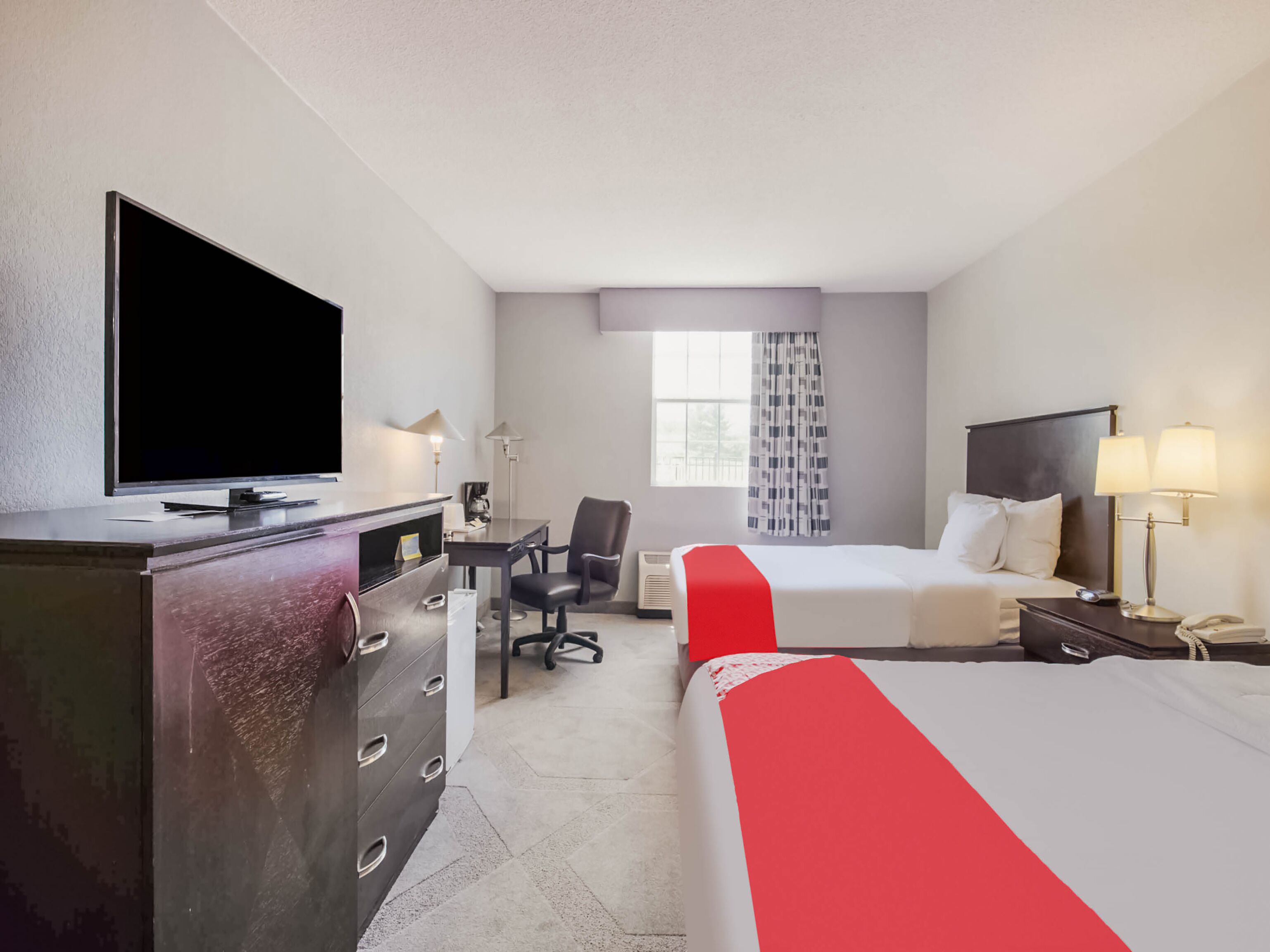A hotel room with a bed, a desk with a chair, a television, and a dresser.