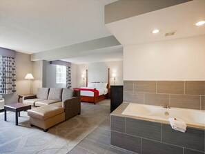 A modern hotel room with a large bed, a sitting area with a sofa and armchairs, a separate bathroom with a bathtub, and a large window providing natural light. - Days Inn by Wyndham Conneaut (Conneaut)
