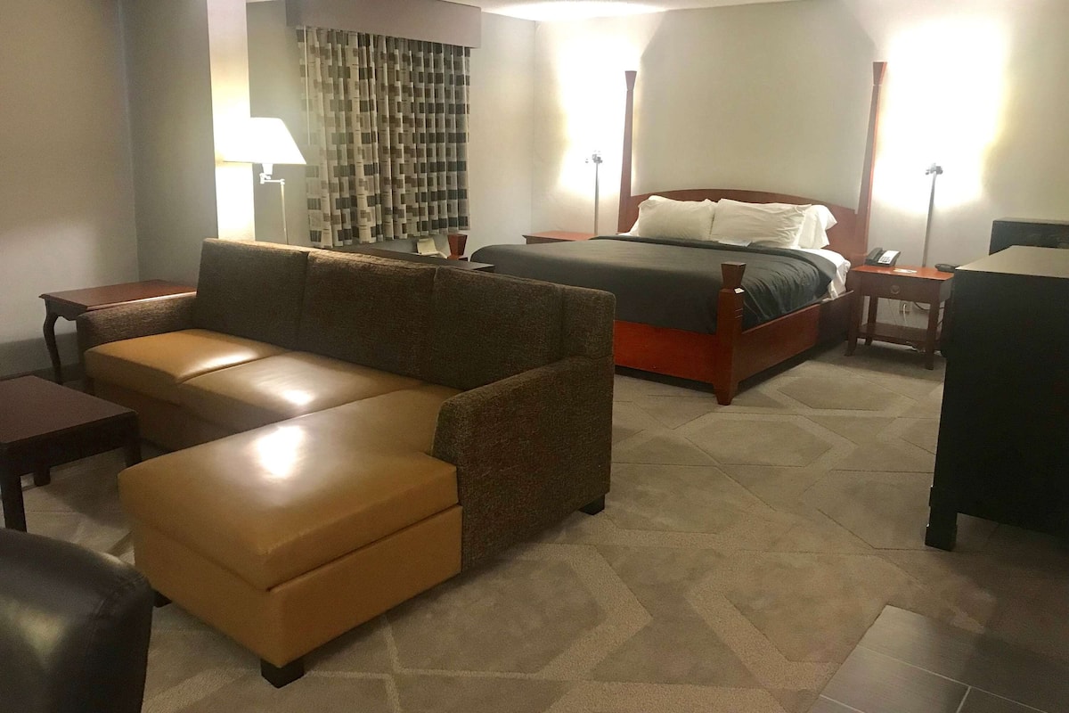 A hotel room with a large bed, a sofa, a desk, and a lamp.