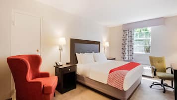 A hotel room with a bed, bedside tables, a red armchair, a green office chair, and a window with curtains.