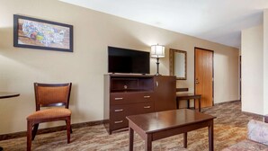 A hotel room with a television, a desk, a chair, a sofa, a dresser, and a mirror.
