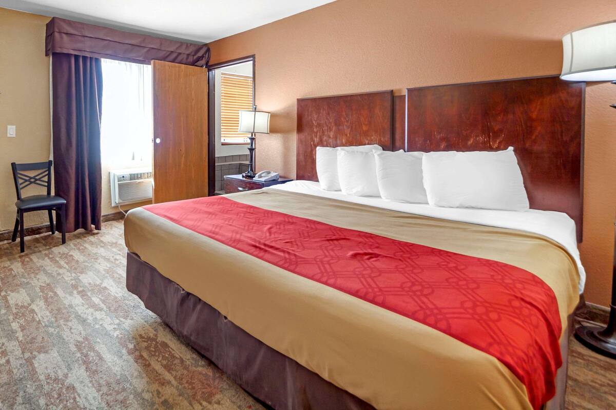 Une chambre d’hôtel avec un grand lit, une chaise, un bureau avec une lampe et une fenêtre avec des rideaux.