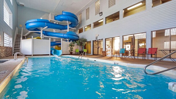 An indoor swimming pool with multiple slides and a seating area with chairs and tables.