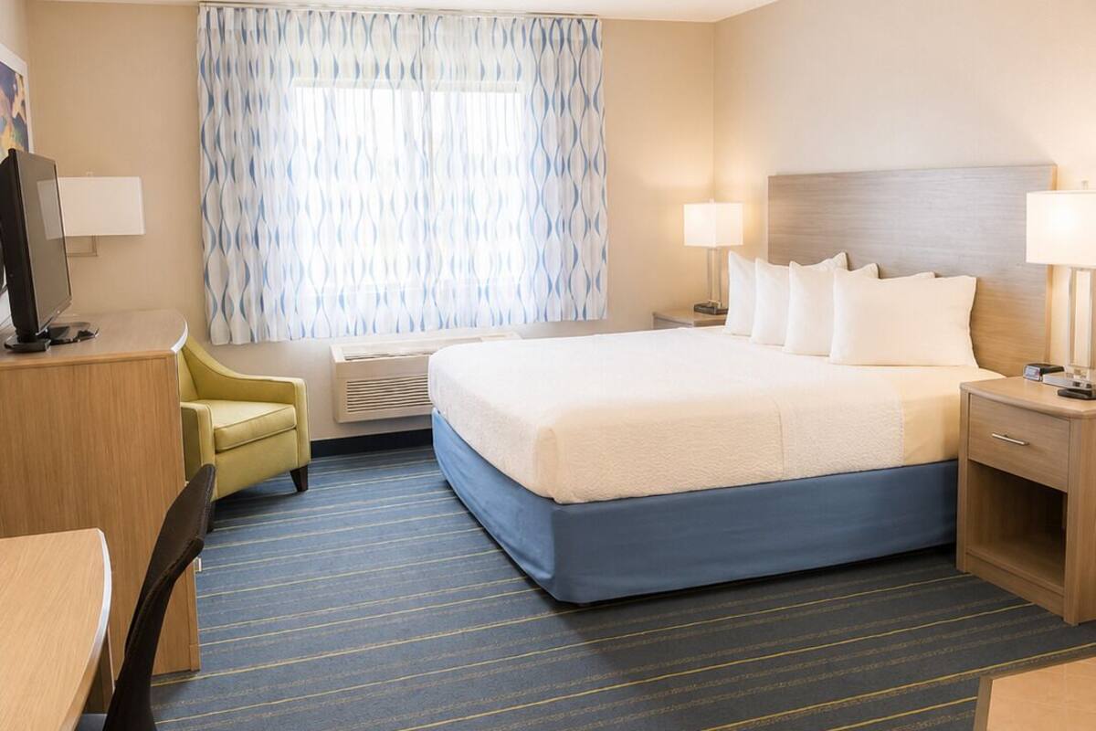 A hotel room with a bed, desk, chair, and a window with curtains.