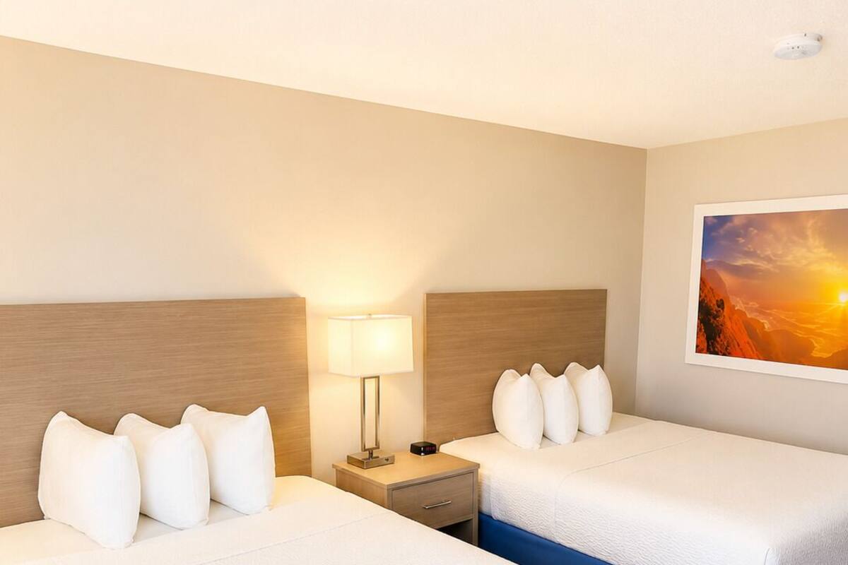 A hotel room with two beds, a nightstand, a lamp, and a painting on the wall.