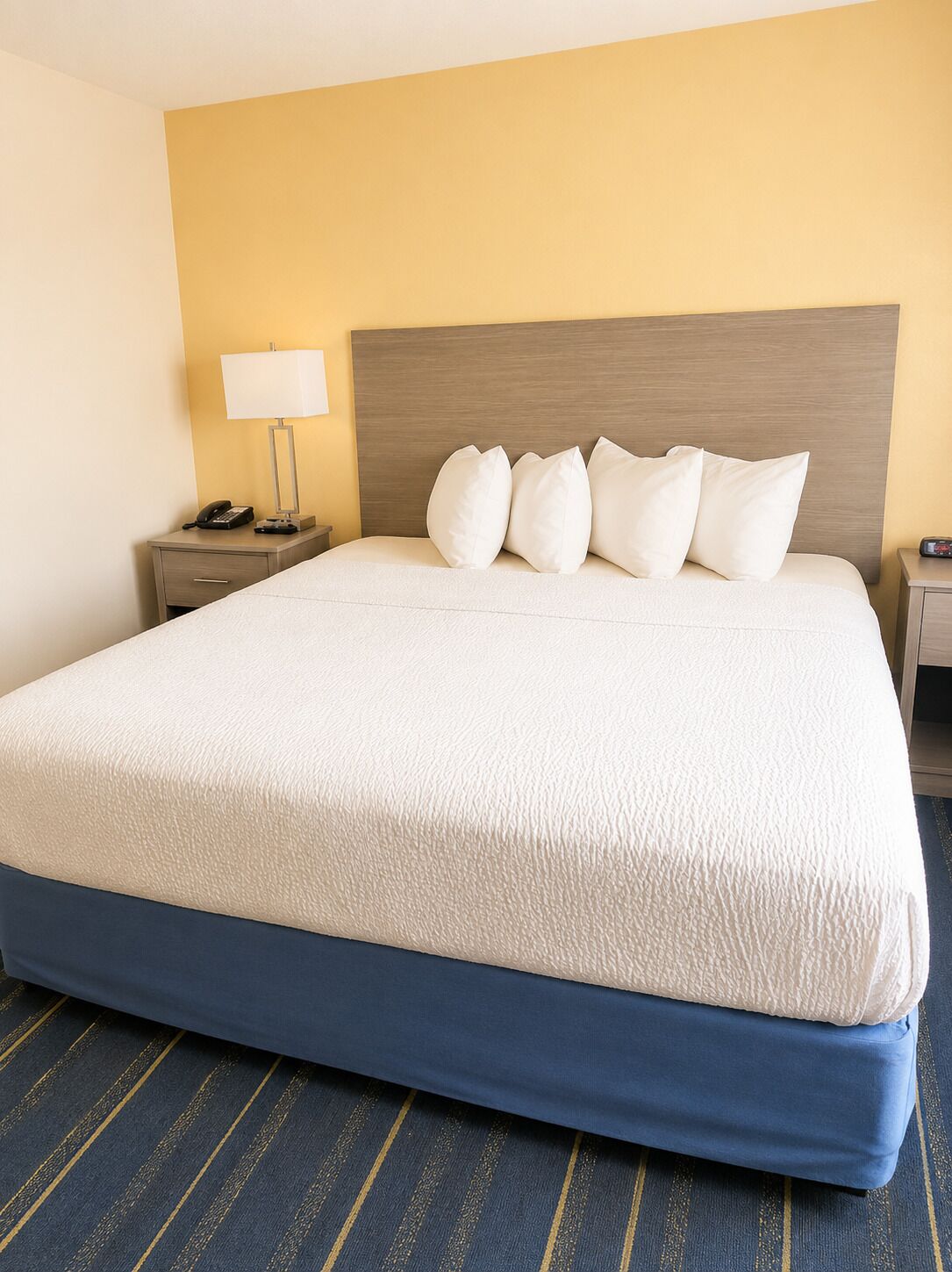 A hotel room with a large bed, a nightstand with a lamp, and a phone.