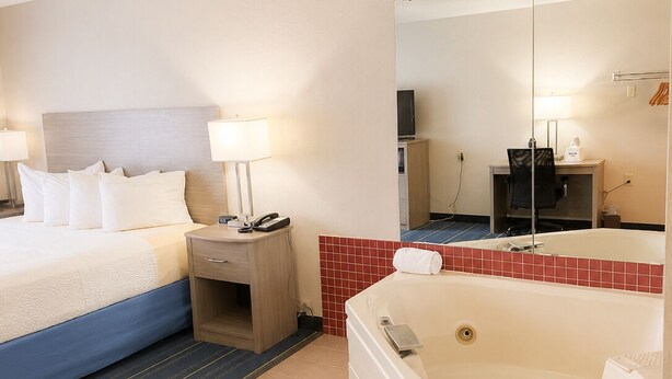 A hotel room with a bed, bedside table, lamp, TV, and a bathtub. - Days Inn by Wyndham Hinckley (Hinckley)