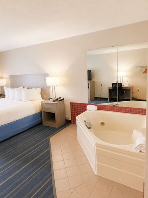 Ein Hotelzimmer mit Bett, Nachttisch, Lampe, Fernseher und einer Badewanne.