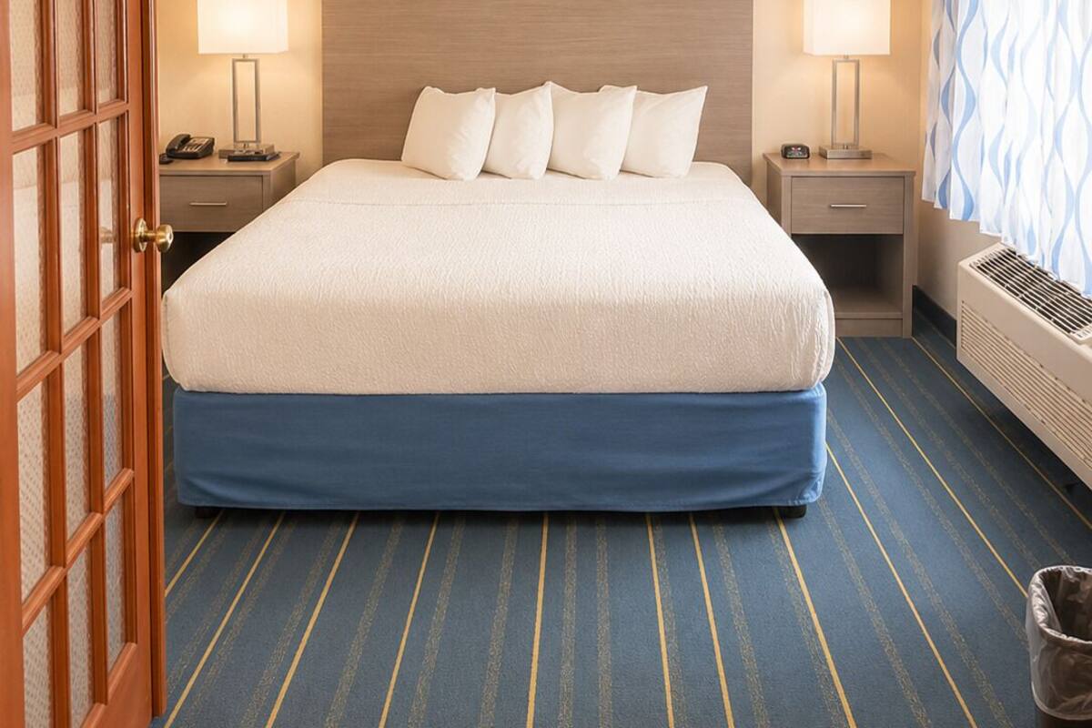 A hotel room with a large bed, two bedside tables with lamps, a wooden door, and a patterned curtain.