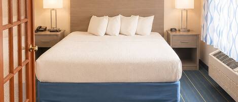 A hotel room with a large bed, two bedside tables with lamps, a wooden door, and a patterned curtain.