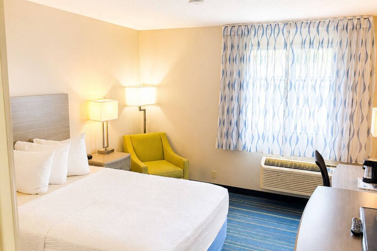 A hotel room with a bed, a desk, a chair, two lamps, and a patterned curtain.
