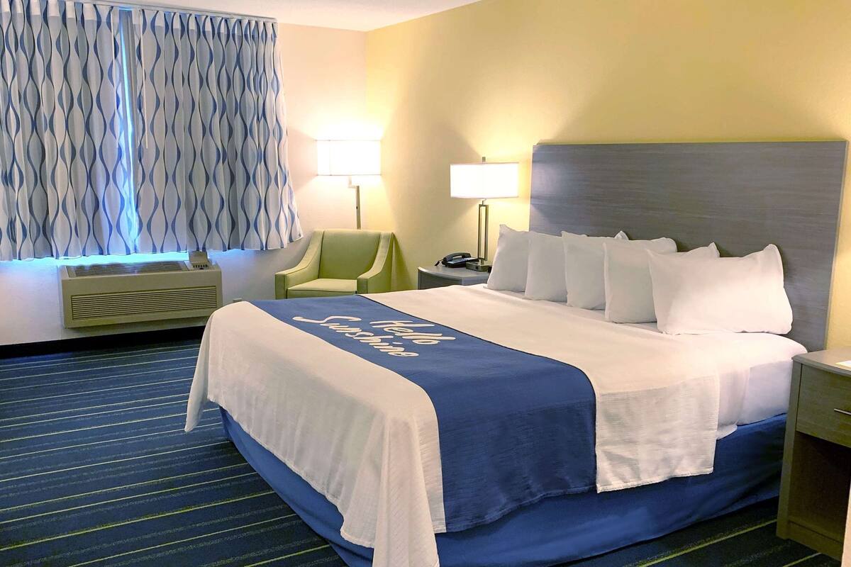 A hotel room with a bed, a chair, a nightstand, a lamp, and a window with curtains.