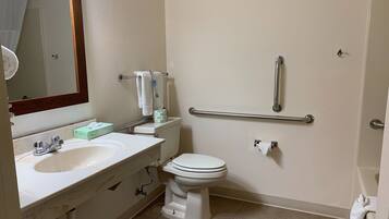 A bathroom with a white sink, mirror, toilet, and grab bars.