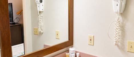 A bathroom with a sink, mirror, hairdryer, and a towel dispenser.
